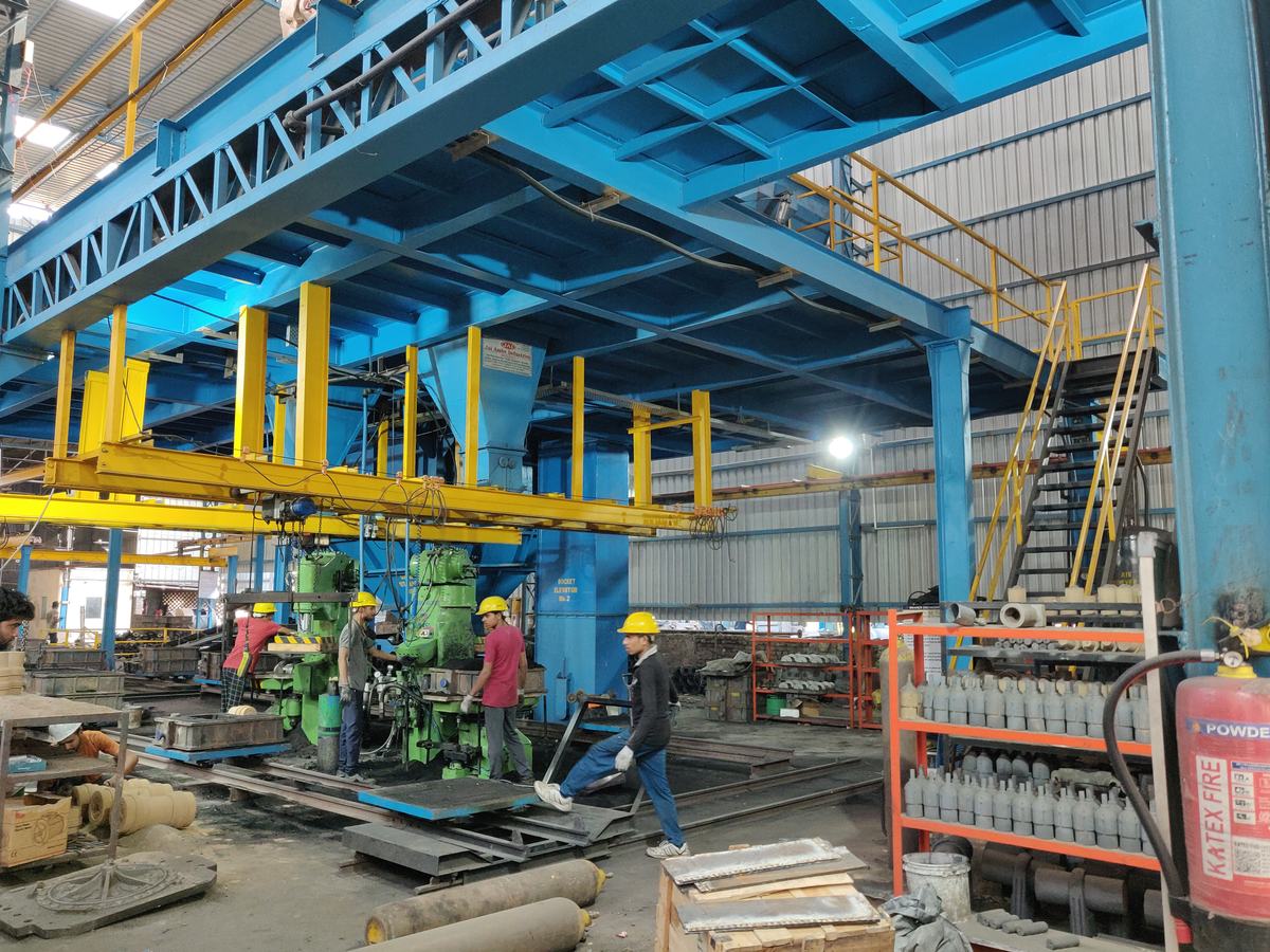 Workers in yellow helmets at green moulding machines under a blue steel gantry in the Bikaner Engineering Works plant